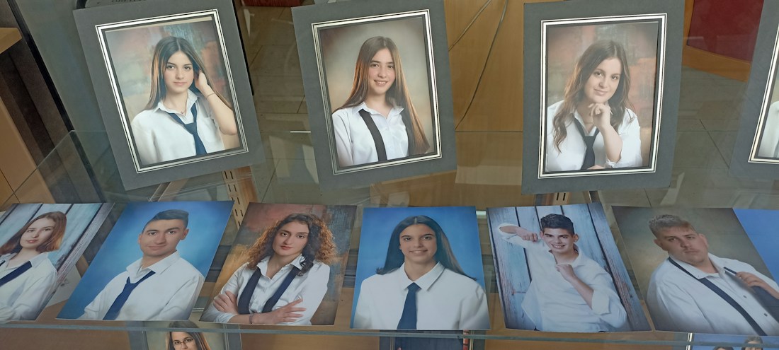 A collection of framed and unframed portrait photographs displayed on a glass surface, primarily featuring young adults in formal attire, likely school or graduation photos. The images show individuals wearing white shirts and dark ties, suggesting a uniform or dress code.