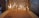 Numerous thin candles are lit and standing upright in a bed of sand, casting a warm and peaceful glow against a textured stone background.