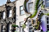 The building facade features a large, intricate dragon sculpture winding across it, displaying vibrant greens and blues. Next to it, the word 'DARK ANGEL' is displayed alongside a stylized figure of a woman, adding a mystical and edgy aesthetic. Below, a sign indicates the presence of a 'CHINESE BUFFET'.