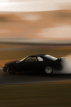 A dynamic shot of a car drifting on a track, dust and smoke swirling around.
