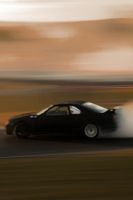 Dynamic photo of a car drifting on a race track with smoke trailing.