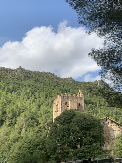 A majestic castle tower surrounded by lush green forest under a bright blue sky.