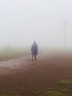 A shadowy figure in a trench coat walking down a foggy street.