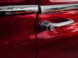 Close-up of a red car's freshly repaired door panel shining under workshop lights.