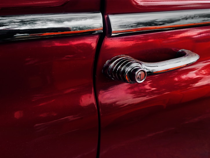 Close-up of a freshly painted car door with a glossy red finish under bright workshop lighting