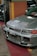 A silver car is parked indoors with a visible license plate reading 'BMM 737'. The vehicle's front grille and hood vents are prominently displayed, and the environment suggests an indoor showroom or parking area with colorful walls in the background.