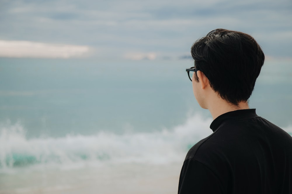 ein Mann, der an einem Strand steht und auf das Meer schaut