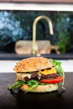 Chef preparing a gourmet burger with fresh ingredients in an open kitchen.