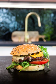 Chef preparing a gourmet burger with fresh ingredients in an open kitchen.