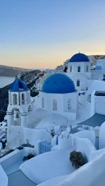A vibrant Greek coastal village with whitewashed houses and blue domes under a clear sky.