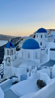 A serene Greek seaside village with whitewashed buildings and blue domes under a clear sky.