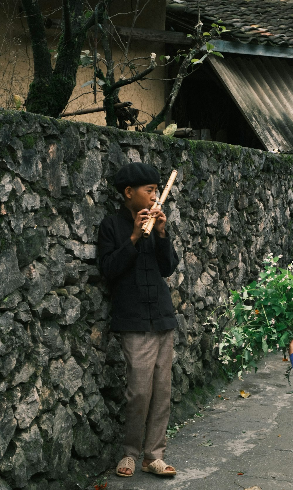 a young boy standing next to a stone wall holding a baseball bat