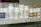 A shelf filled with various bottles of medication, each labeled with different drug names and dosages. The labels are primarily white with some colorful accents. The bottles vary in size and shape, typical of a pharmacy or medical supply setting.