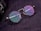 A pair of round eyeglasses with tortoiseshell frames and colorful reflective lenses is placed on a textured dark surface. The glasses are next to a part of a camera lens which is partially visible on the edge of the image.