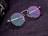 A pair of round eyeglasses with tortoiseshell frames and colorful reflective lenses is placed on a textured dark surface. The glasses are next to a part of a camera lens which is partially visible on the edge of the image.