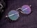 A pair of round eyeglasses with tortoiseshell frames and colorful reflective lenses is placed on a textured dark surface. The glasses are next to a part of a camera lens which is partially visible on the edge of the image.