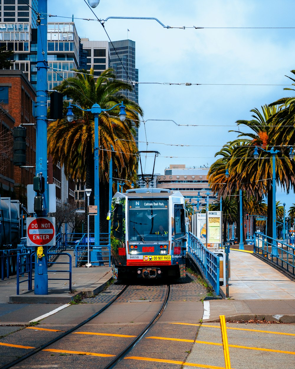 a red and white train traveling down tracks next to palm trees