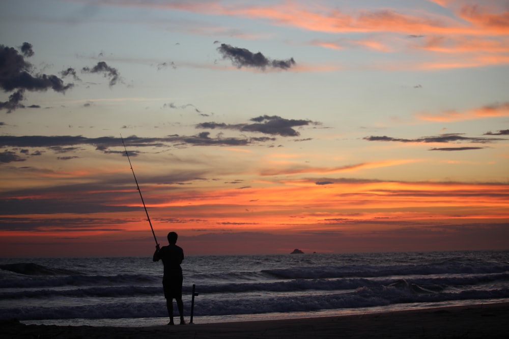 a man standing on a beach holding a fishing pole