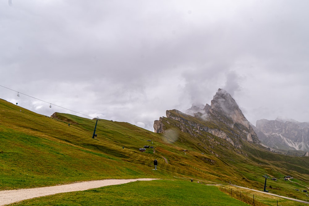 a path going up a grassy hill with a mountain in the background