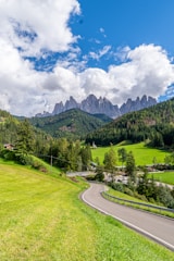A colorful landscape photograph featuring a winding road through lush greenery under a bright sky.