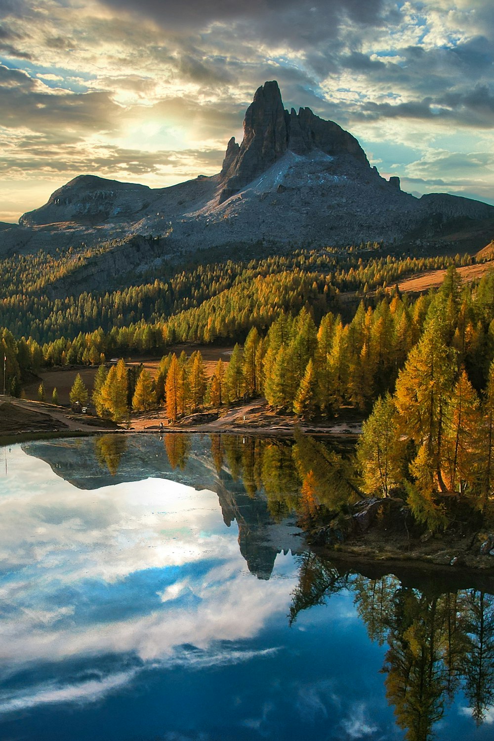 a lake surrounded by trees and mountains under a cloudy sky