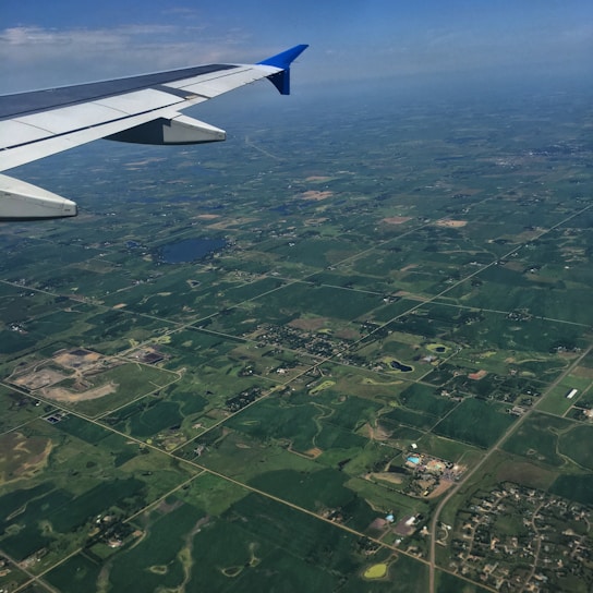 A serene aerial view of lush green farm plots with wide roads and modern infrastructure under a clear sky.