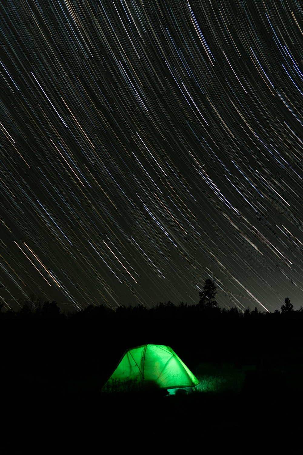 a green tent sitting in the middle of a field under a star filled sky