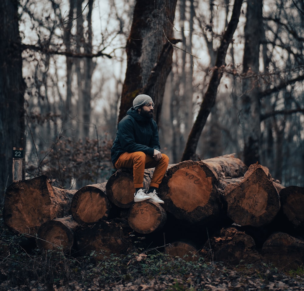 a man sitting on a pile of logs in the woods