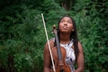 a woman holding a violin in front of a forest