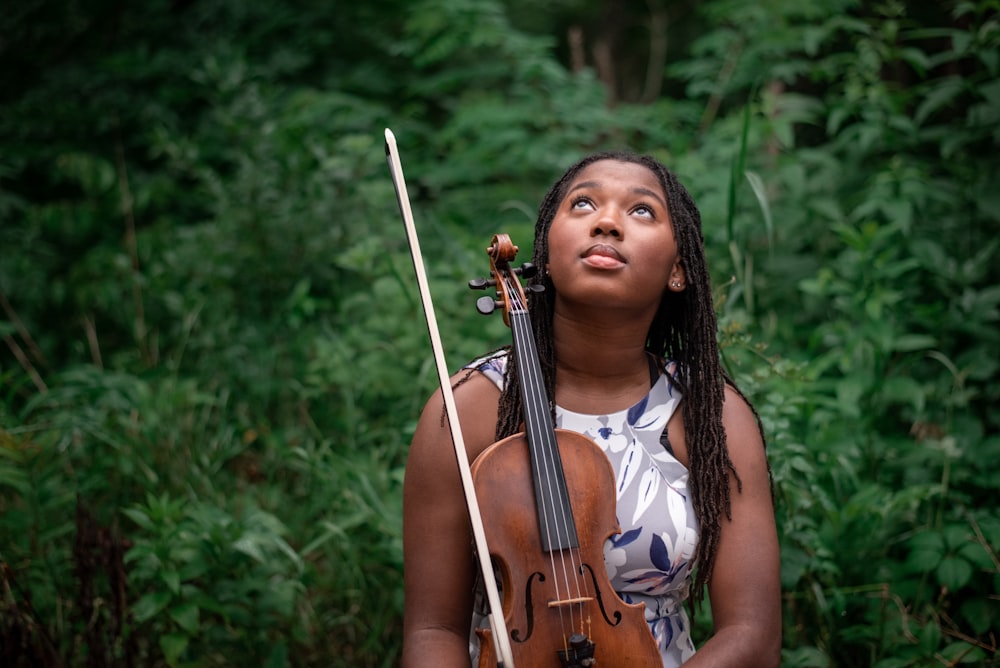 a woman holding a violin in front of a forest