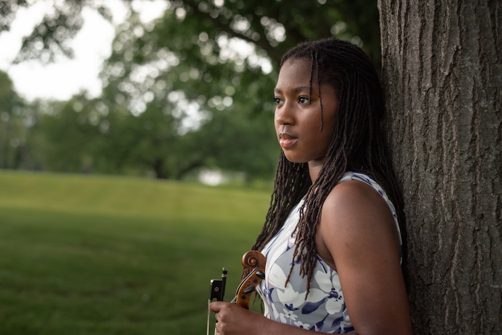 a woman leaning against a tree holding a violin