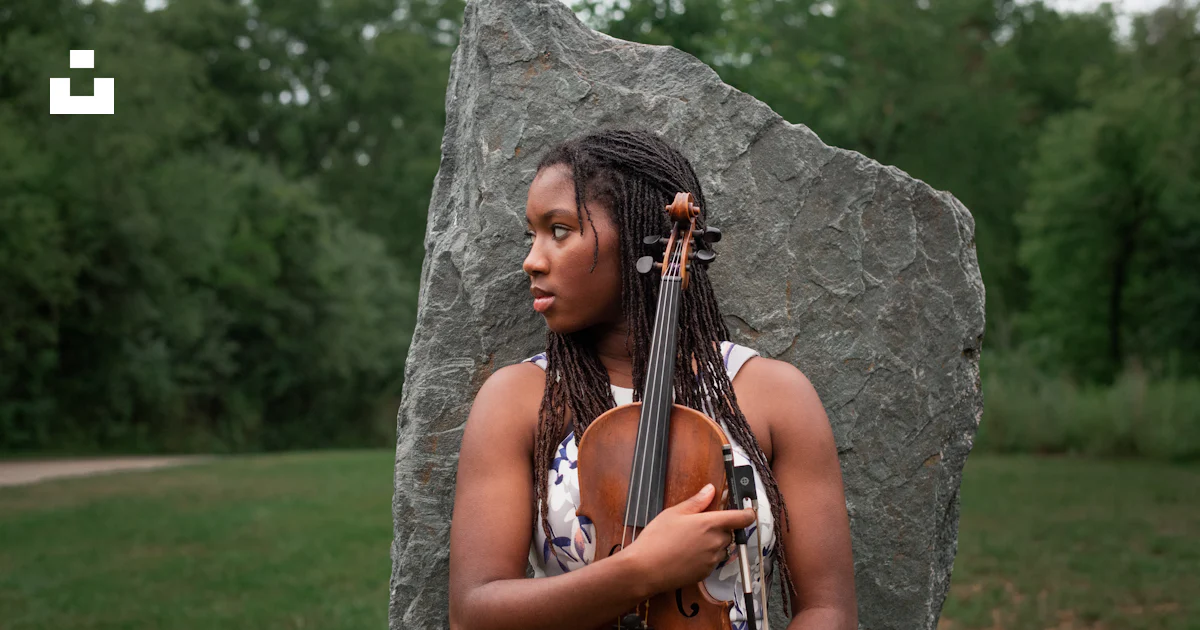 A woman with dreadlocks holding a violin in front of a rock photo ...