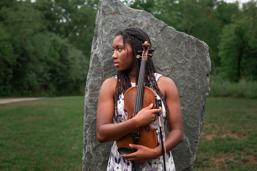 a woman with dreadlocks holding a violin in front of a rock