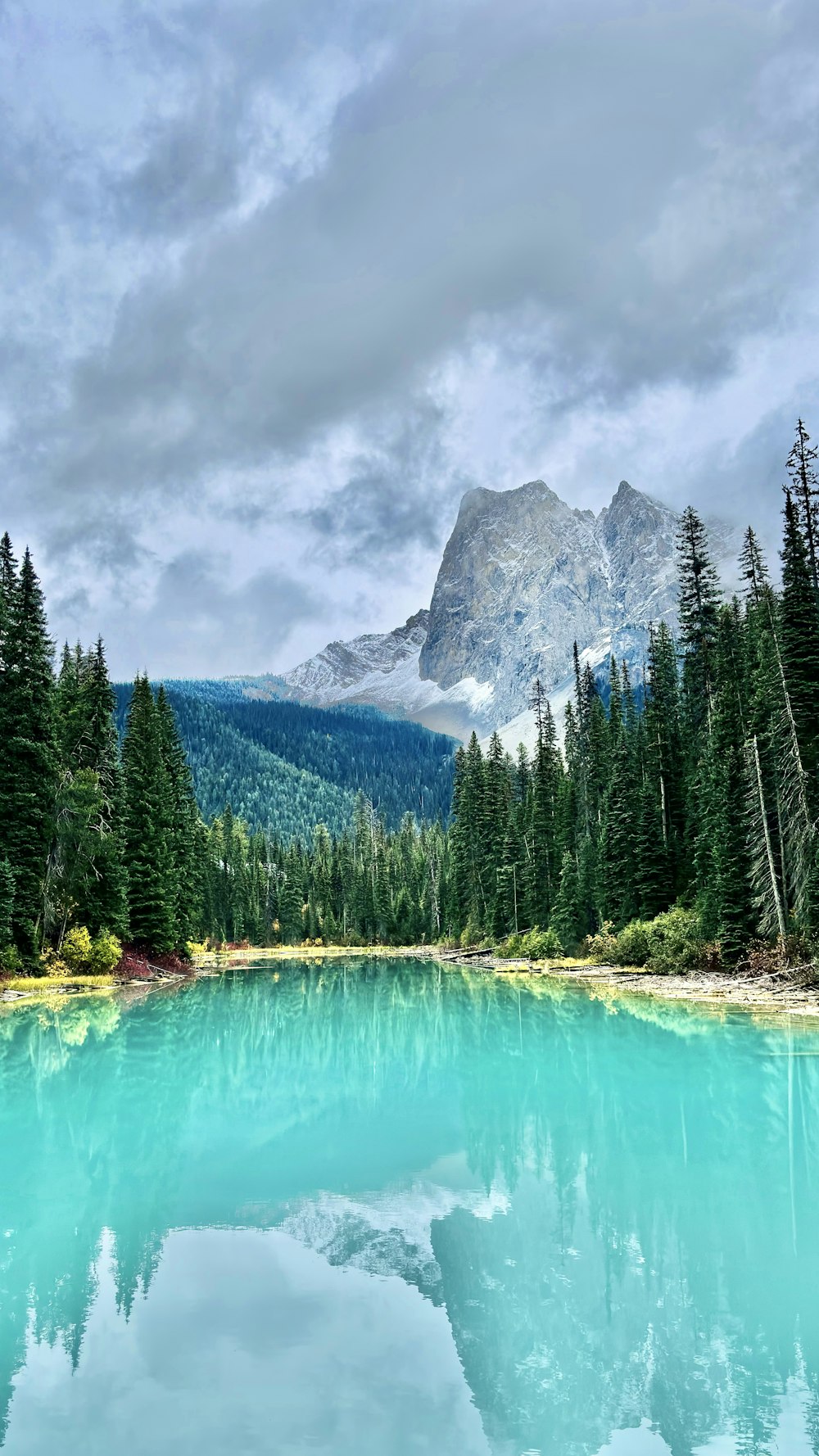 a lake surrounded by trees and mountains under a cloudy sky