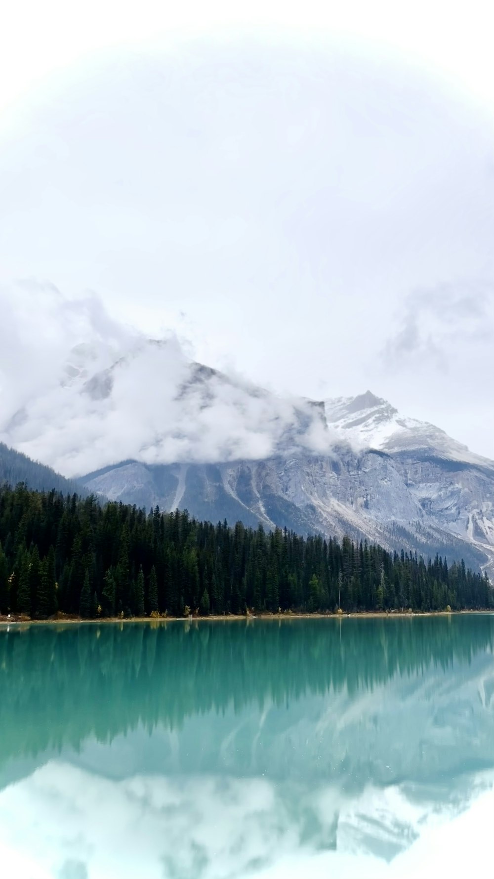 um lago cercado por montanhas e árvores sob um céu nublado