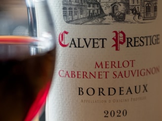 Close-up of a wine bottle label showing the name Calvet Prestige, Merlot, Cabernet Sauvignon, Bordeaux, and the year 2020. A glass of red wine is partially visible to the left.