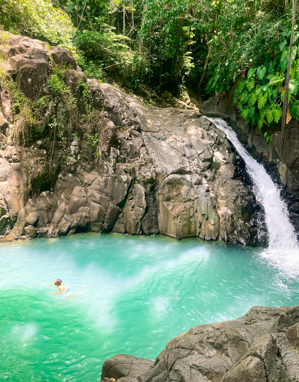 a man swimming in a pool of water near a waterfall