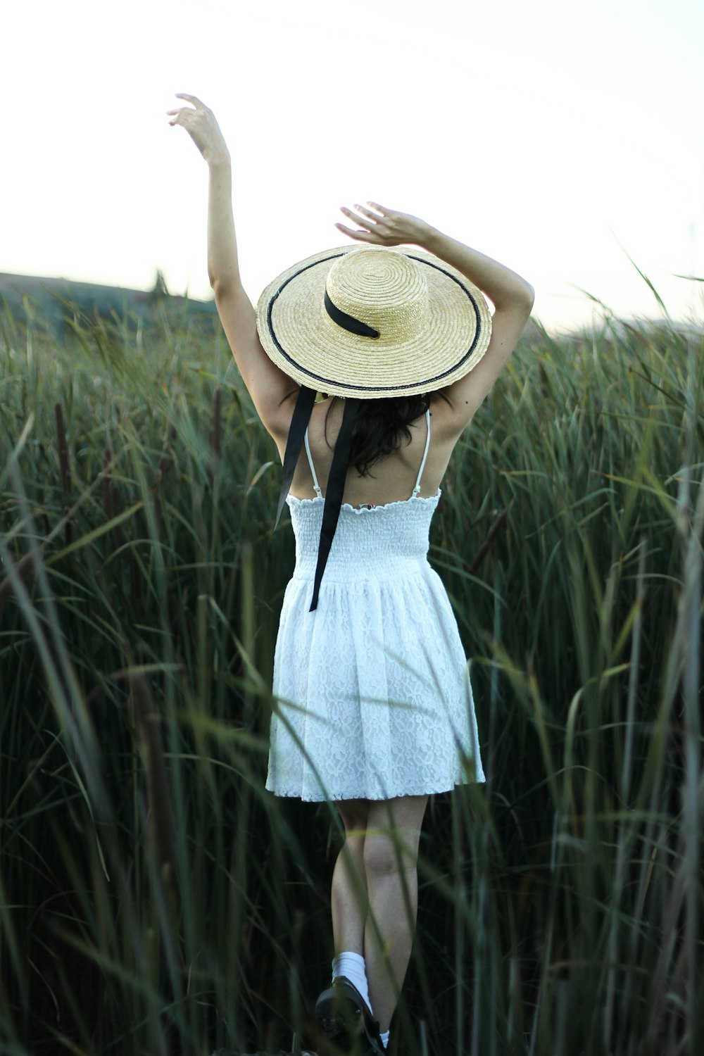 a woman in a white dress and straw hat walking through tall grass