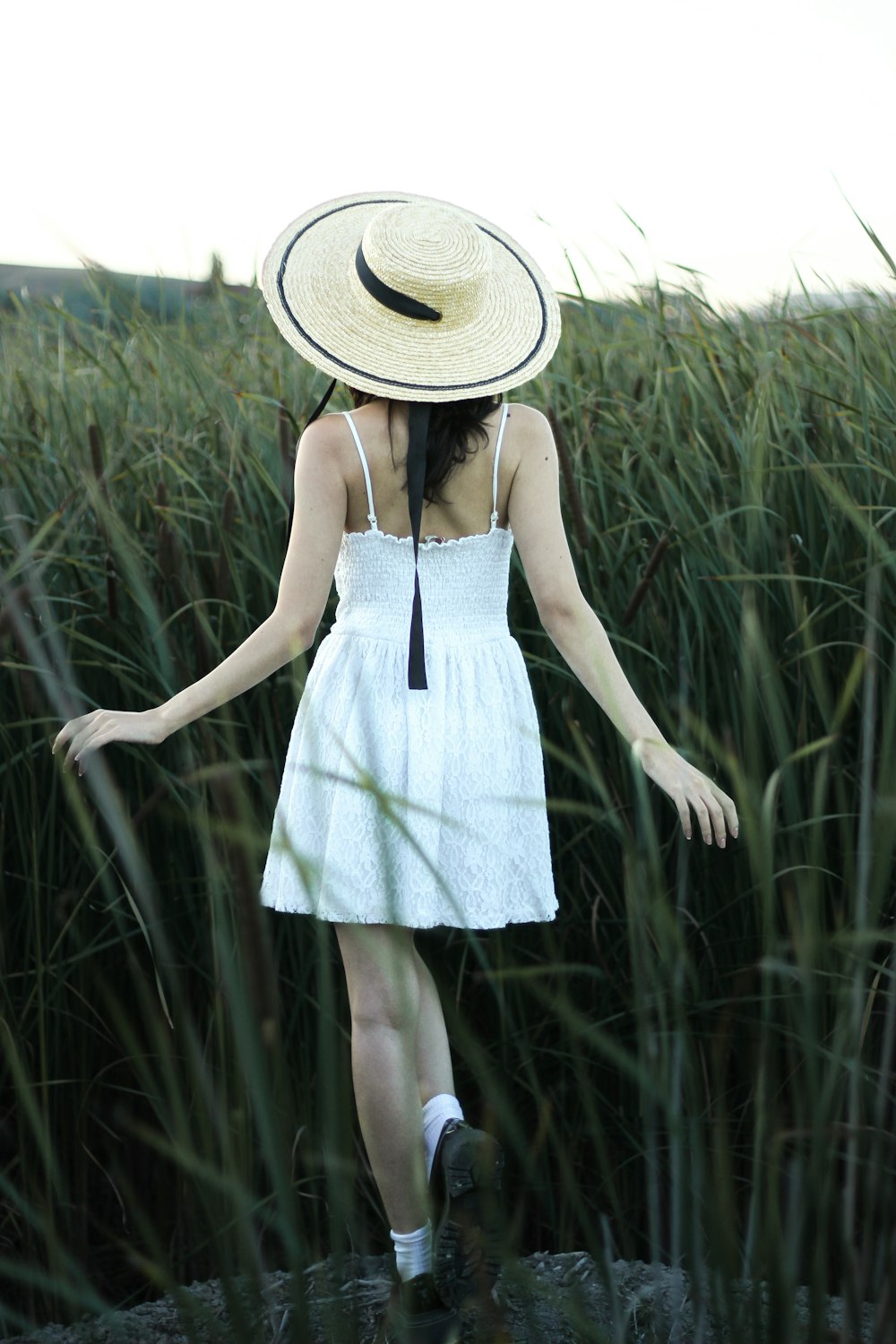 a woman in a hat walks through tall grass
