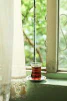 A quiet moment of a woman sipping tea by a window, sunlight filtering through sheer curtains.