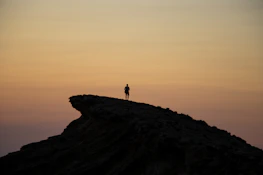 Silhouette of a lone figure standing atop a rugged cliff overlooking a vast Mesopotamian landscape at dusk.