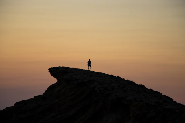 A focused man standing at dawn on a rocky cliff, symbolizing strength and new beginnings.
