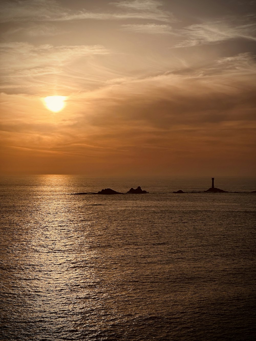 the sun is setting over the ocean with a lighthouse in the distance