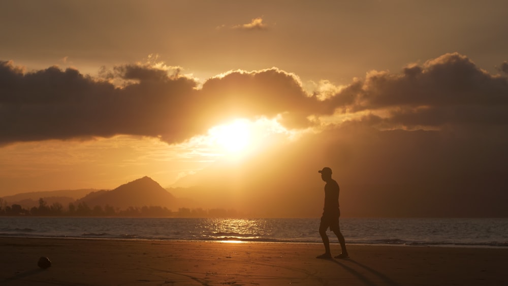 a man walking on a beach at sunset
