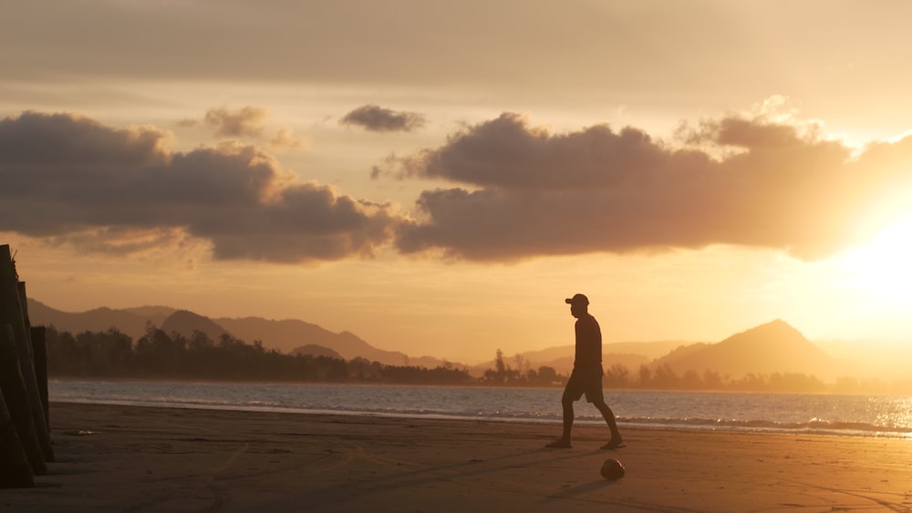 a man walking on the beach at sunset