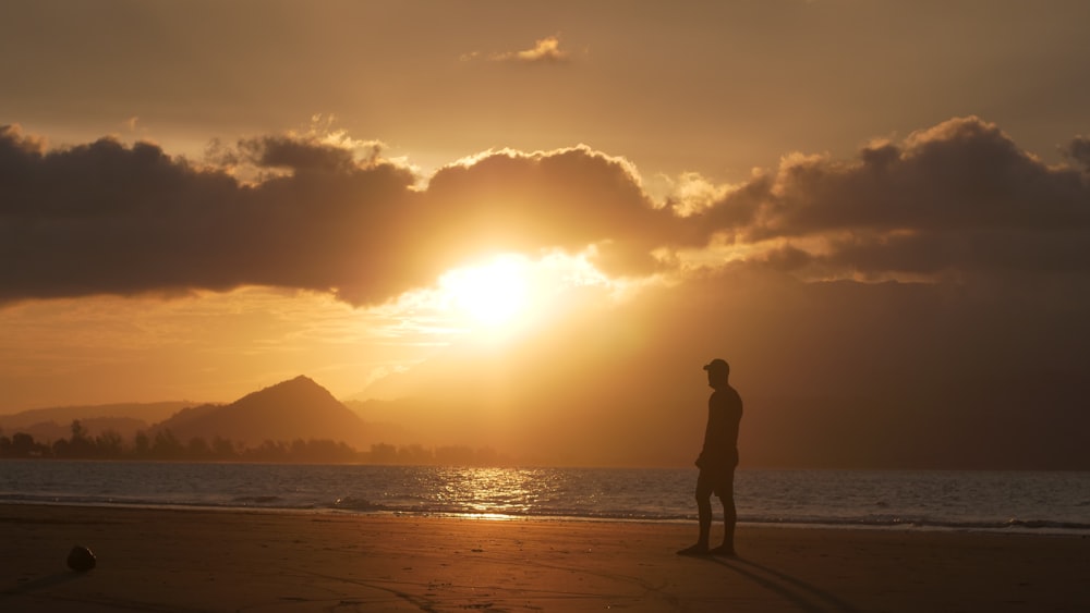 a man standing on a beach at sunset