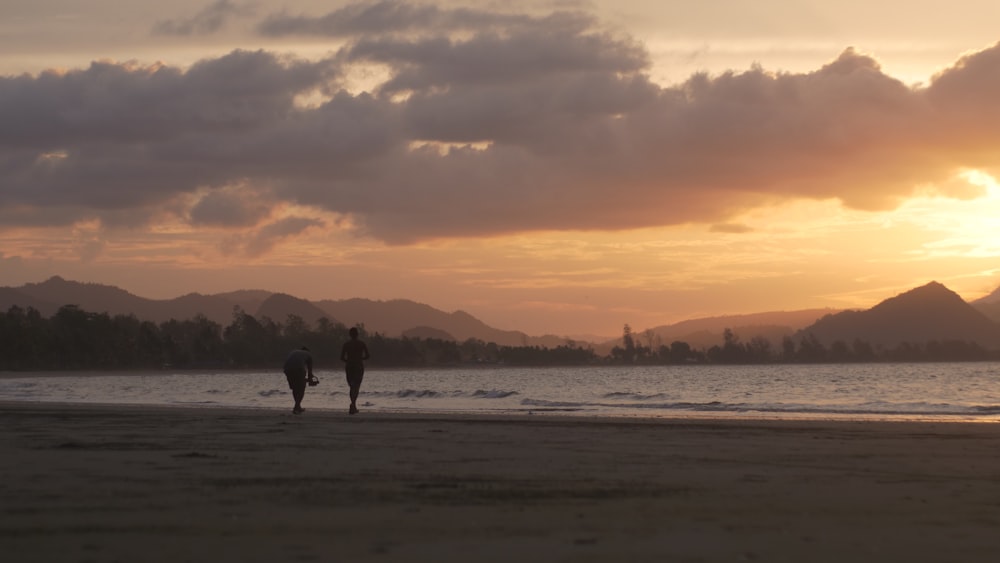 two people walking on a beach at sunset