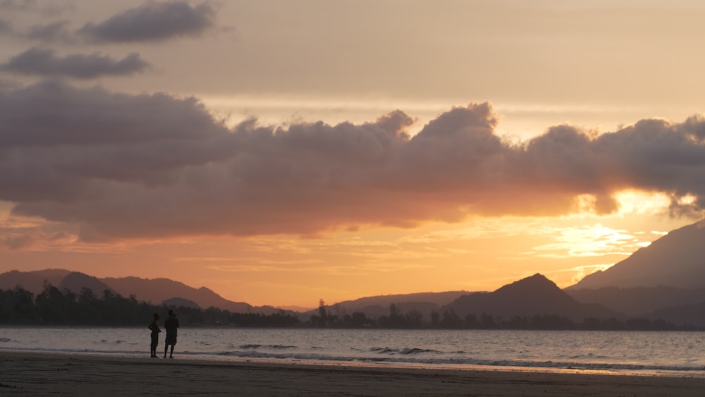 two people standing on a beach at sunset