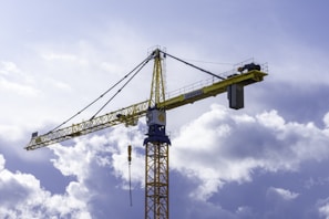 A yellow heavy-duty crane lifting steel beams on a construction site under overcast skies.