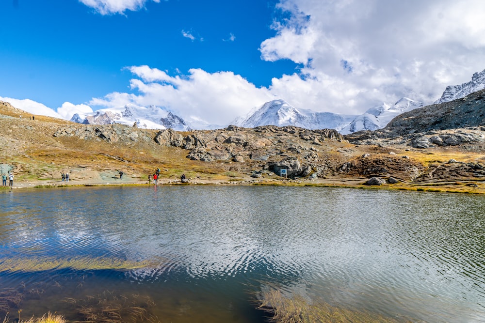 um grupo de pessoas em pé ao lado de uma montanha ao lado de um lago